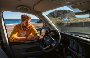 Mann mit Handy in der Hand vor einem VW Bulli