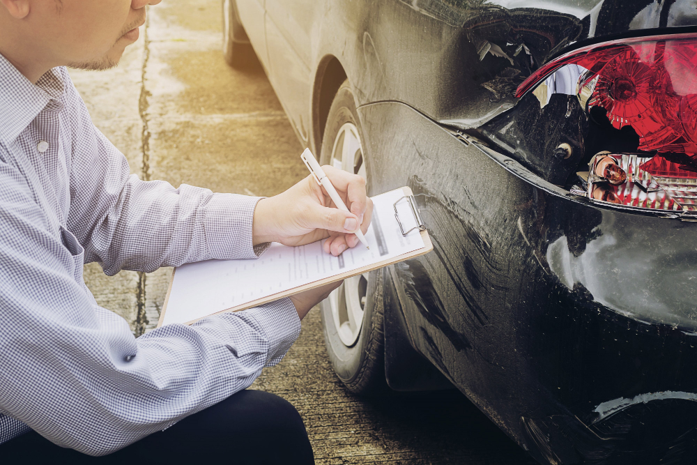 Mann begutachtet Unfallwagen und macht sich Notizen | Autounfall was tun